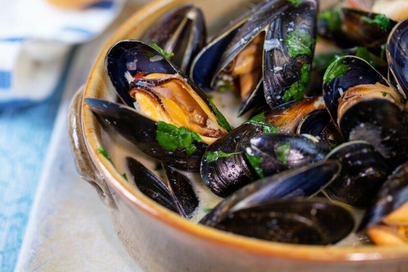 A large bowl with cooked oysters in broth. Many of the oysters have opened and are ready to eat.