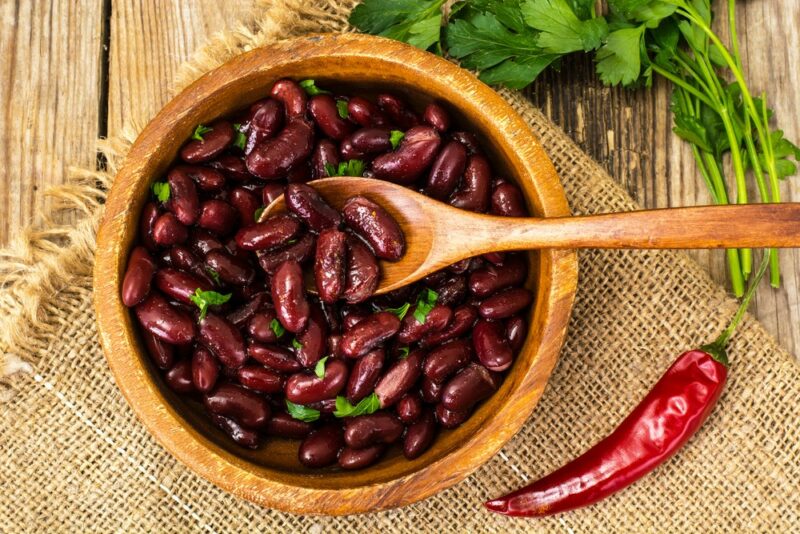 A large bowl of cooked red beans with a wooden spoon, next to a chili pepper