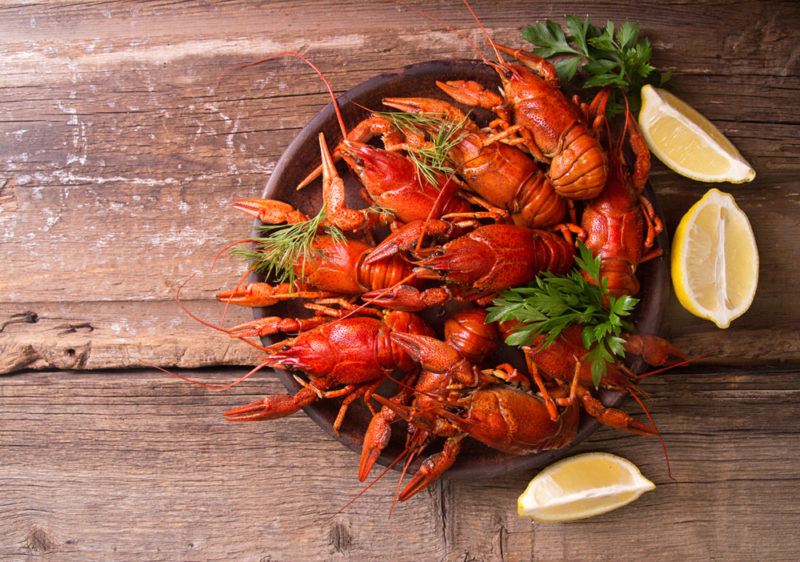 A dark bowl filled with crayfish, ready for a party, with a few lemon wedges just outside of it