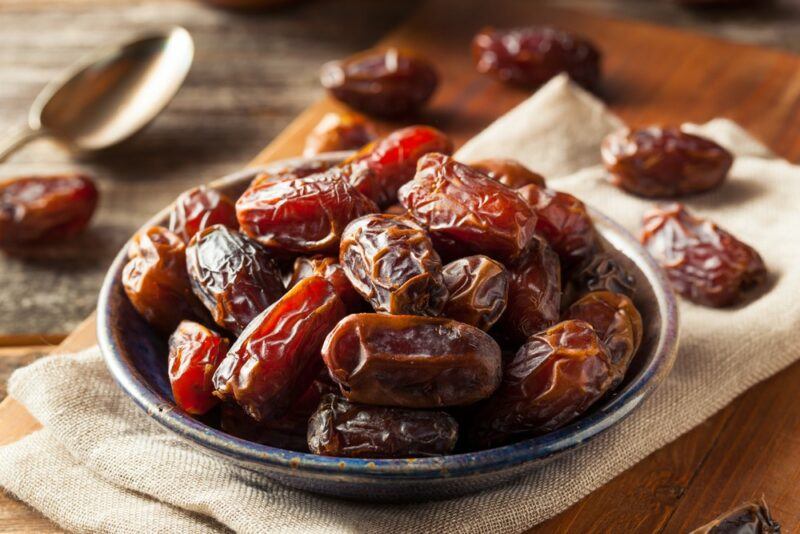 A large bowl of dates, with more dates scattered across a cloth