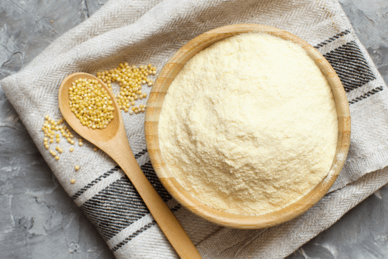 A cloth, on which there is a large bowl of millet flour next to a spoon of millet seeds.