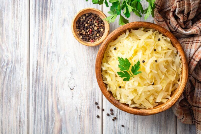 A large brown bowl filled with sauerkraut, next to a small one of peppercorns on a wooden table