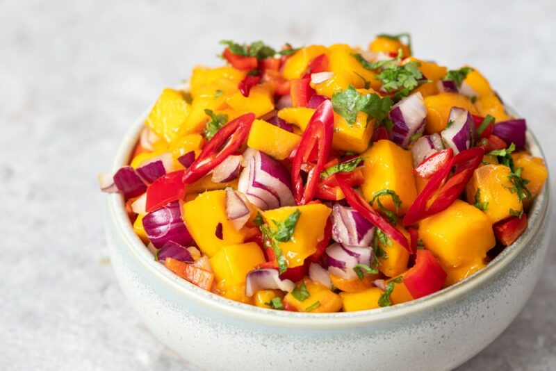 A large blue white bowl containing a mango based salsa that also includes raw red onions