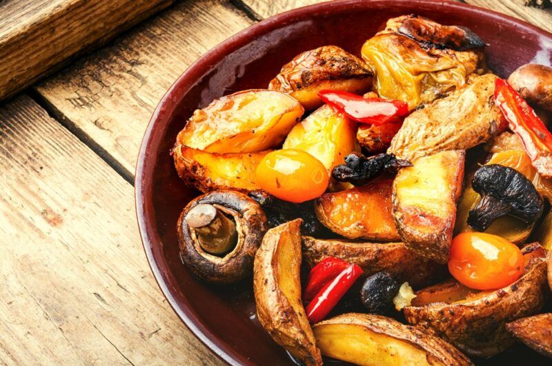 A brown dish containing roasted vegetables and mushrooms