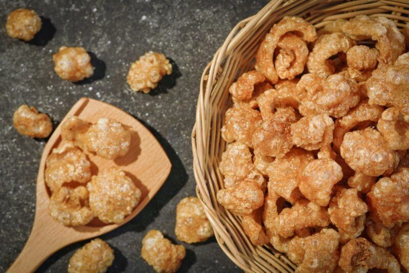 A large cane basket filled with pork rinds, next to a wooden spoon containing more