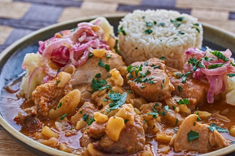 A large black plate containing carapulcra and rice