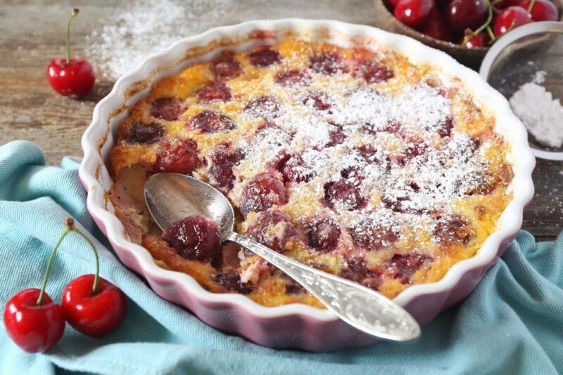 A large white dish containing a cherry clafoutis, on top of a light blue cloth