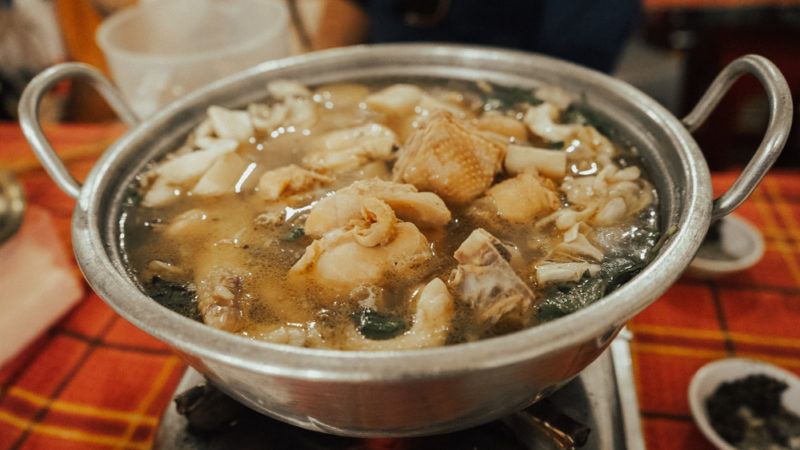 A steel bowl with handles filled with lau, which is a type of communal hot pot meal