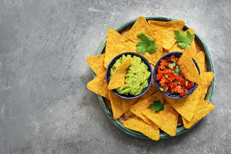 A dish of fresh nacho chips with a small bowl of salsa and another of guacamole in the middle