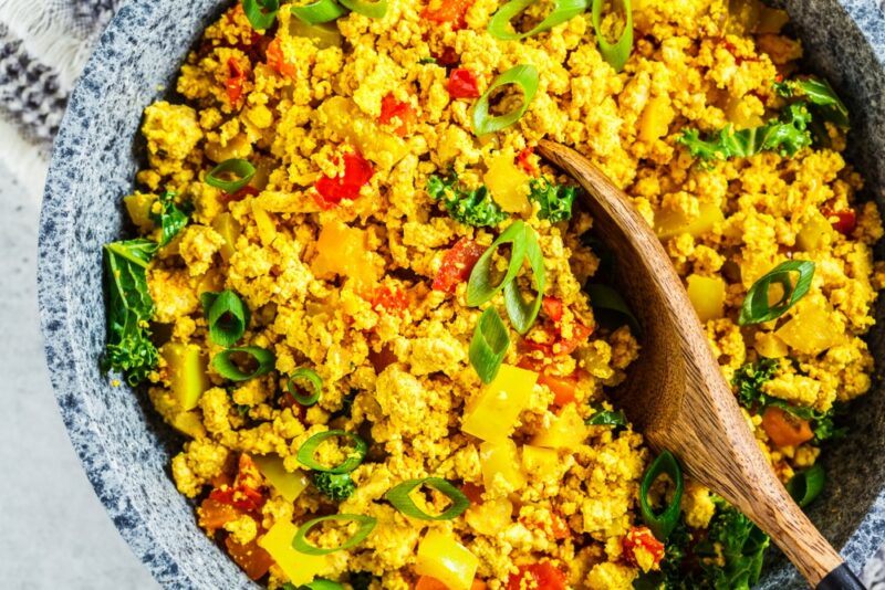 A large dish of tofu scramble with a wooden spoon