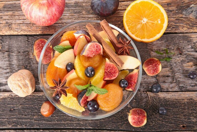 A large glass bowl containing a fall fruit salad with fruit scattered around the outside