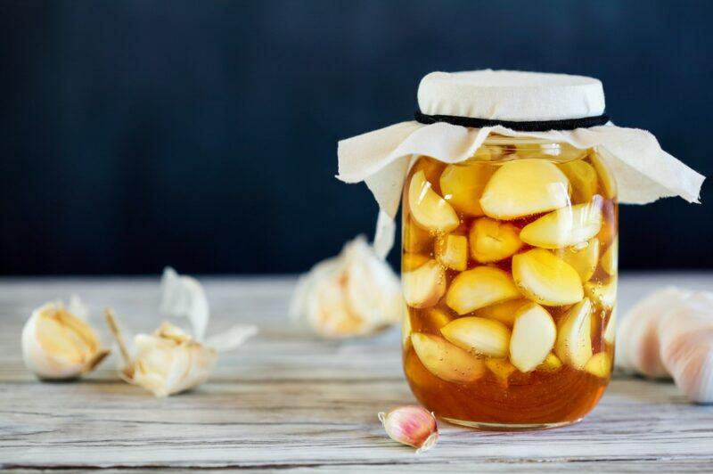 A single large jar of garlic fermenting in honey on a table.