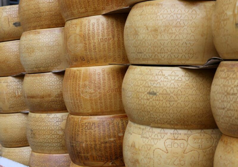 A large number of aged cheese wheels that have been stacked. The different columns of cheese have their own distinct labels