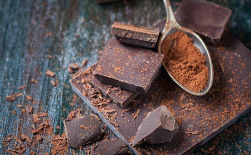 A dark table with pieces of chocolate and a spoon of powder