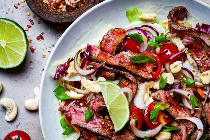 A gray plate with a steak salad, with limes