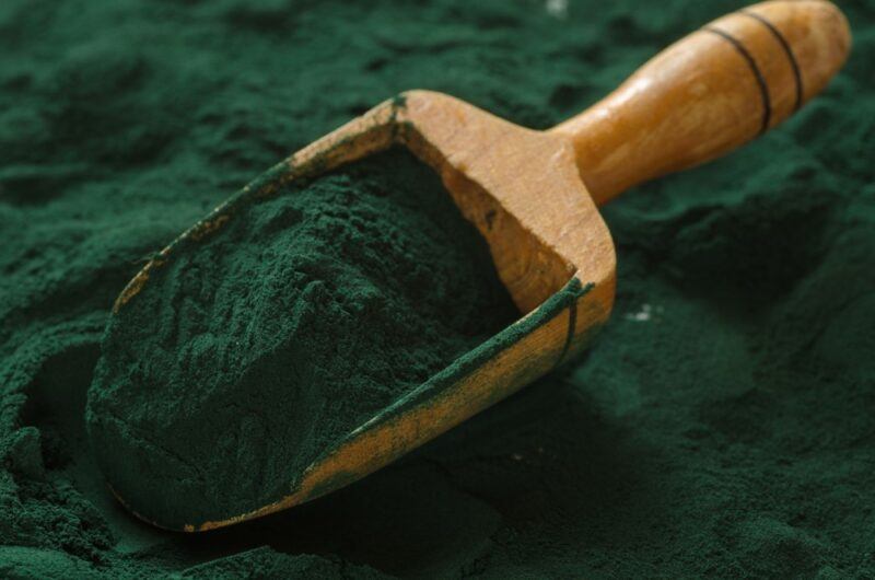 A large amount of spirulina powder on a table, with a wooden scoop