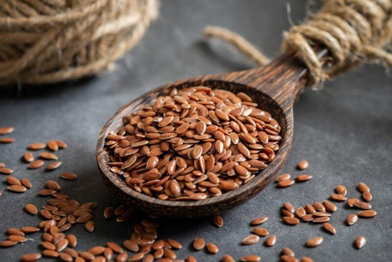 A large wooden spoon filled with flax seeds, with rope around the handle