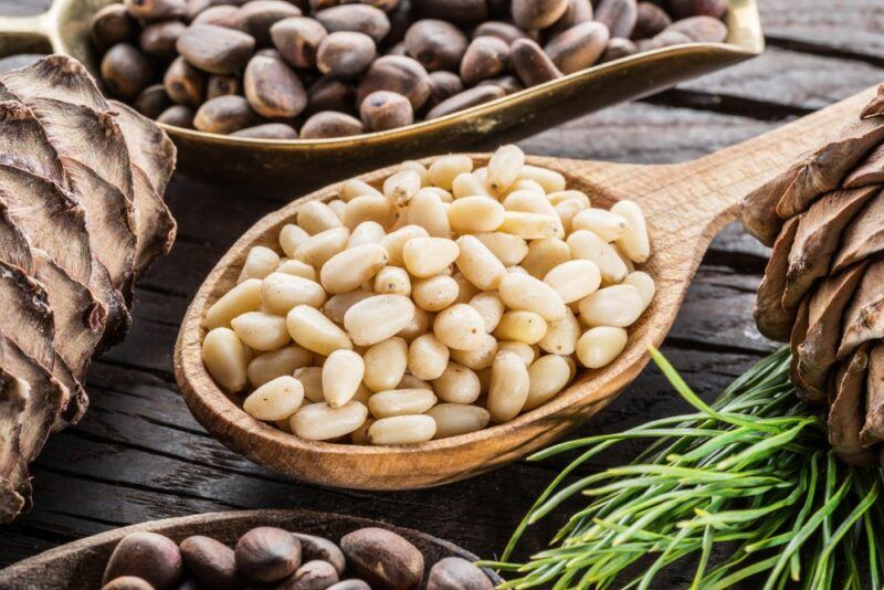 A large wooden spoon of raw pine nuts and another two spoons, partly out of shot, containing pine nuts still in their shell