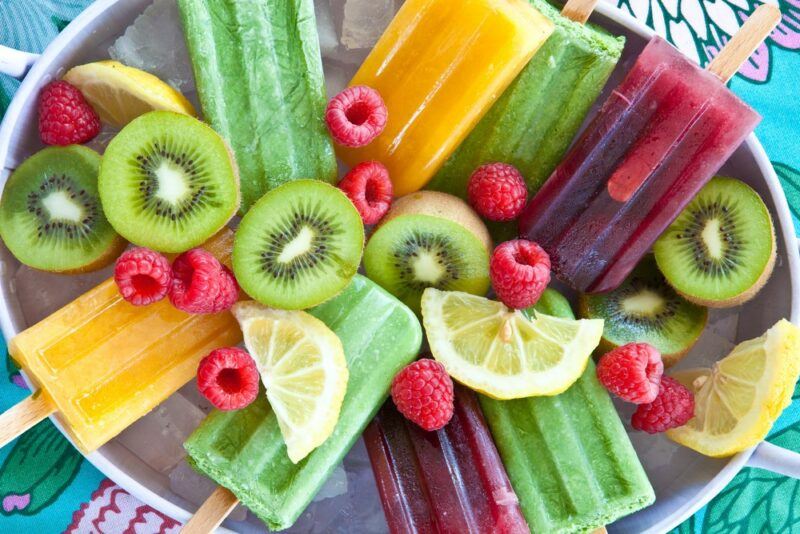 A large tray with homemade fruit popsicles, next to many types of fresh fruit