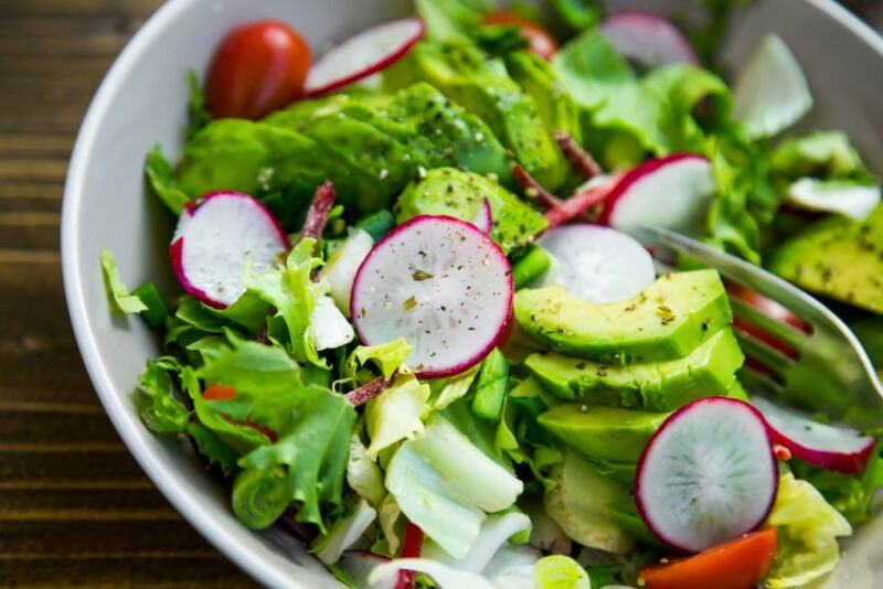 A large white bowl containing a fresh lettuce, radish, tomato, and avocado salad