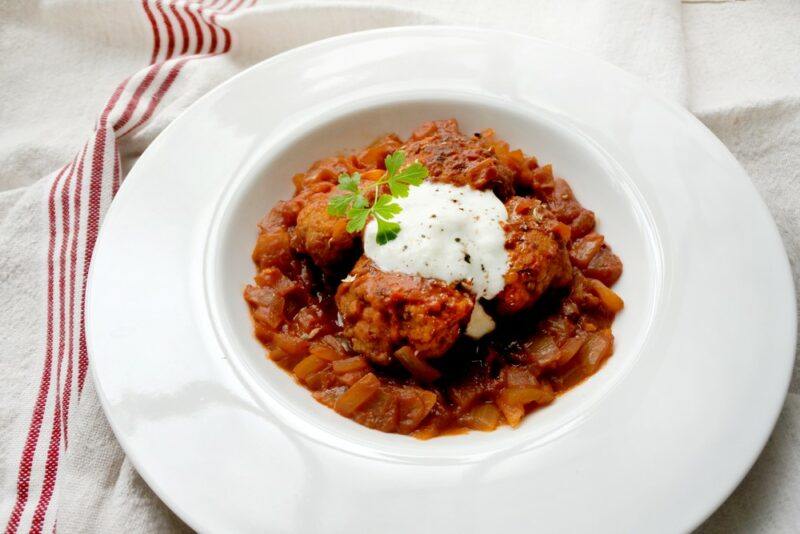 A white bowl filled with albondigas or meatballs, with a dab of sour cream on top