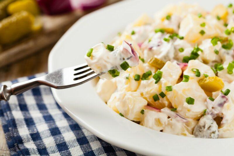 A white tray containing a potato salad with a fork being used to grab a piece