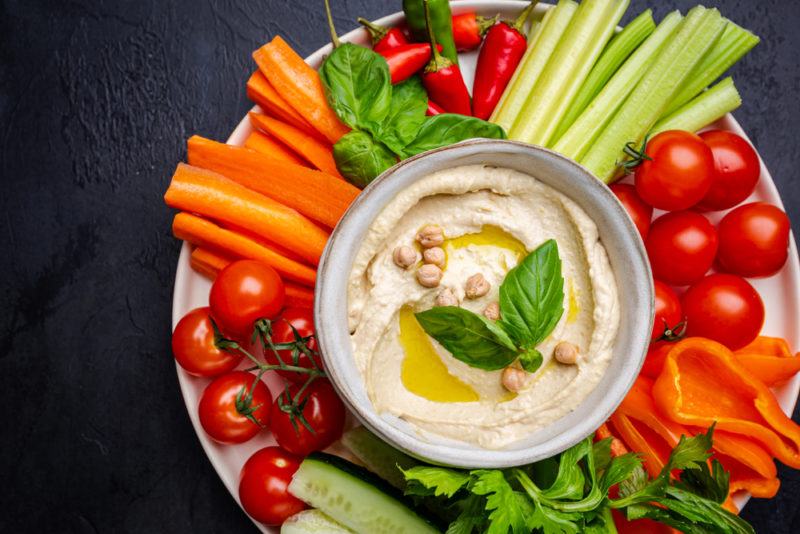 A large white dish with sliced fresh vegetables and a dish of hummus