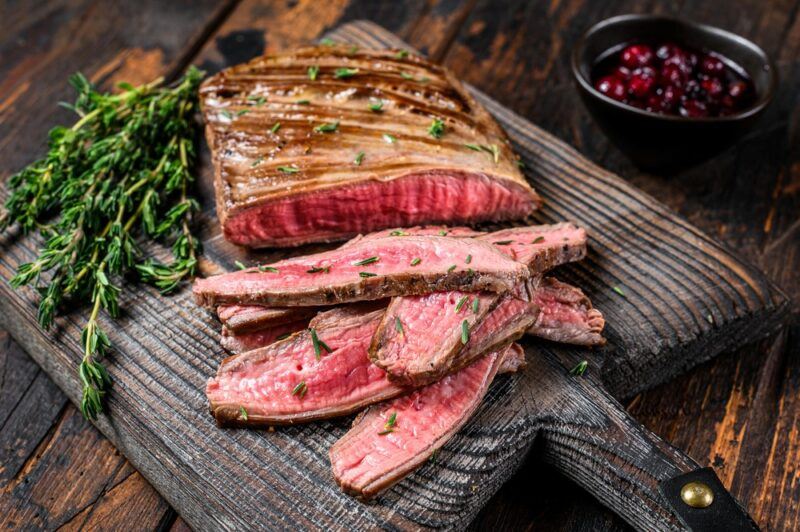 A wooden board containing a large piece of flap steak, where some of it has been sliced into smaller pieces