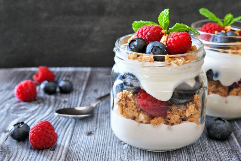 Two glass jars with layered parfaits that include cereal, yogurt and fruit