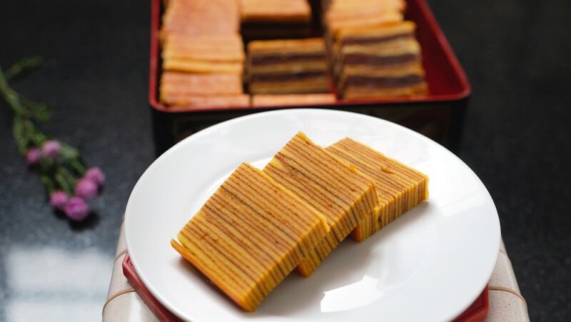 A white plate with three pieces of a layered vanilla and spice cake, with more pieces in the background