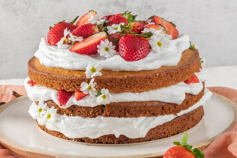 A layered sponge cake with white chocolate filling and fresh strawberries on top