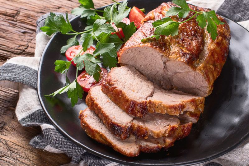 A leg of roast pork that's been partially sliced, with a small salad of greens and tomatoes on the side