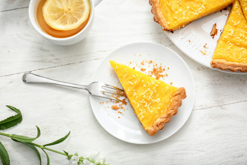 A small white plate with a lemon cake, next to a larger lemon cake with a piece cut out