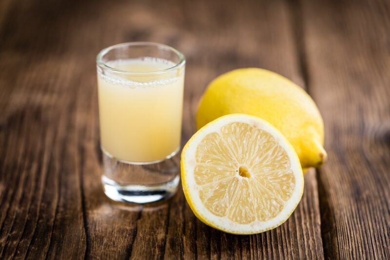 A single lemon drop shot next to a whole lemon and half a lemon