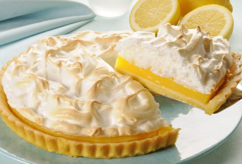 A lemon meringue pie on a blue plate with one piece being lifted out of it