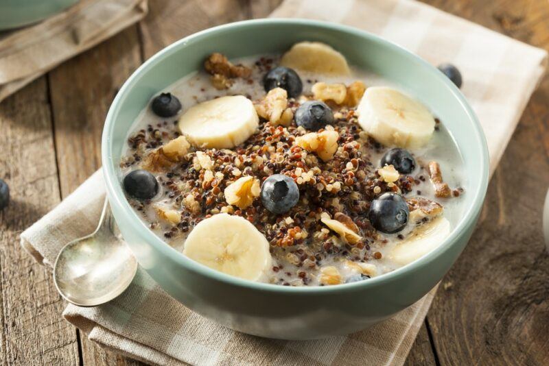 A green or blue bowl of quinoa porridge with blueberries and bananas