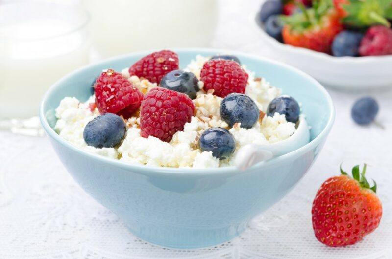 A small blue bowl that contains cottage cheese, blueberries, and raspberries