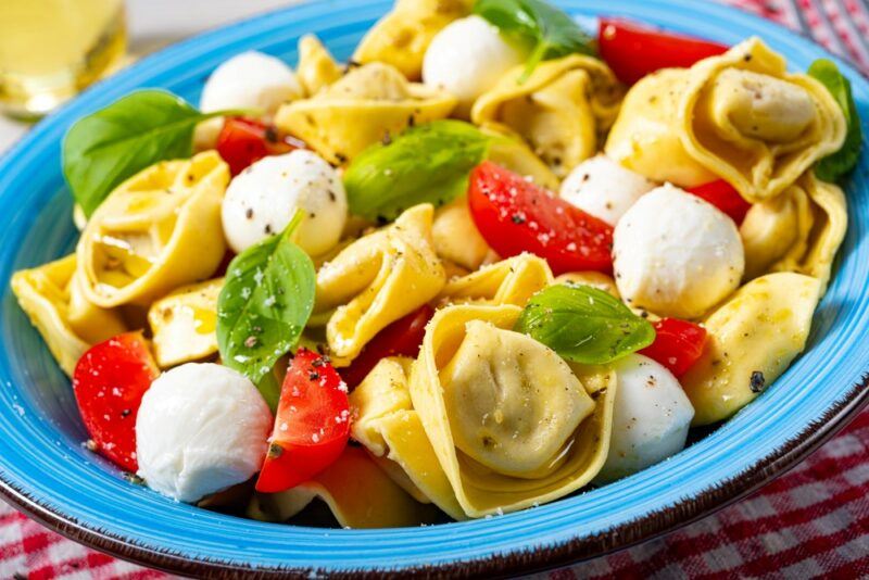 A light blue plate with a tortellini pasta salad that includes cheese and tomatoes