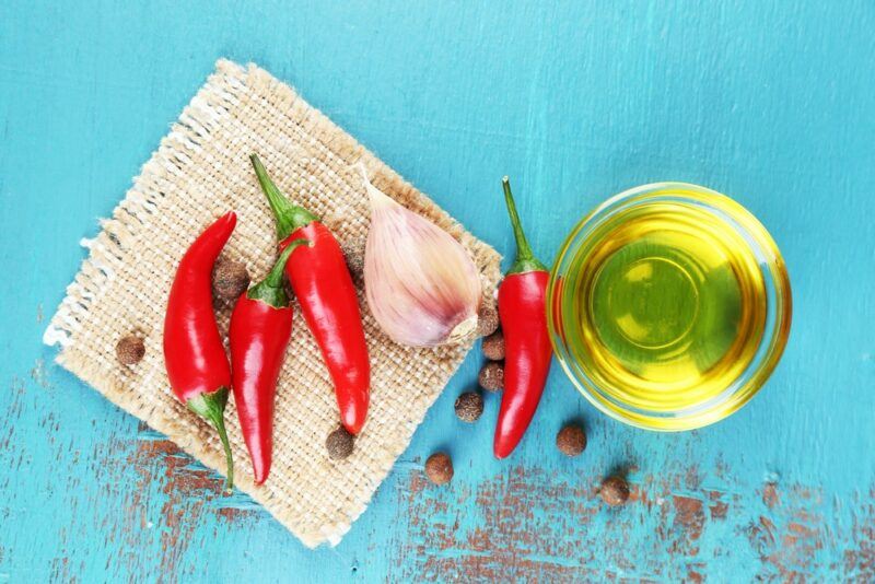 A light blue table with a cloth, fresh chilis, garlic, and pepper corns, next to a bowl of olive oil