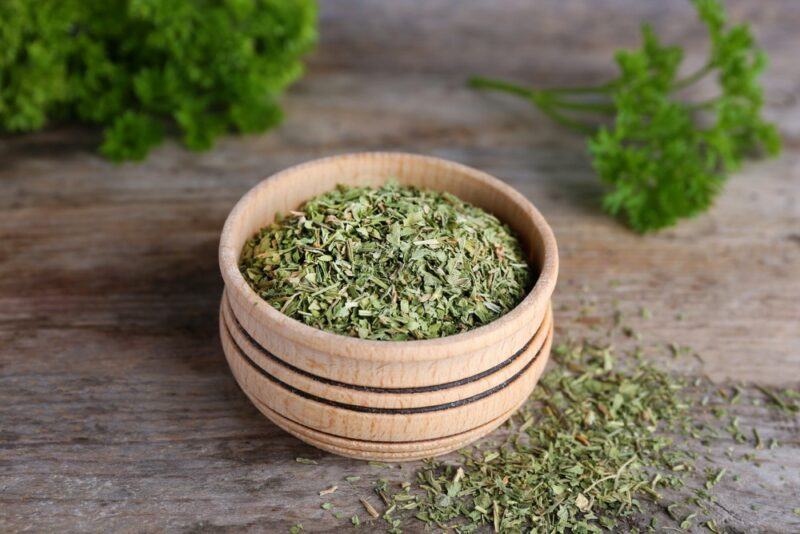 A brown wooden bowl filled with dried parsley