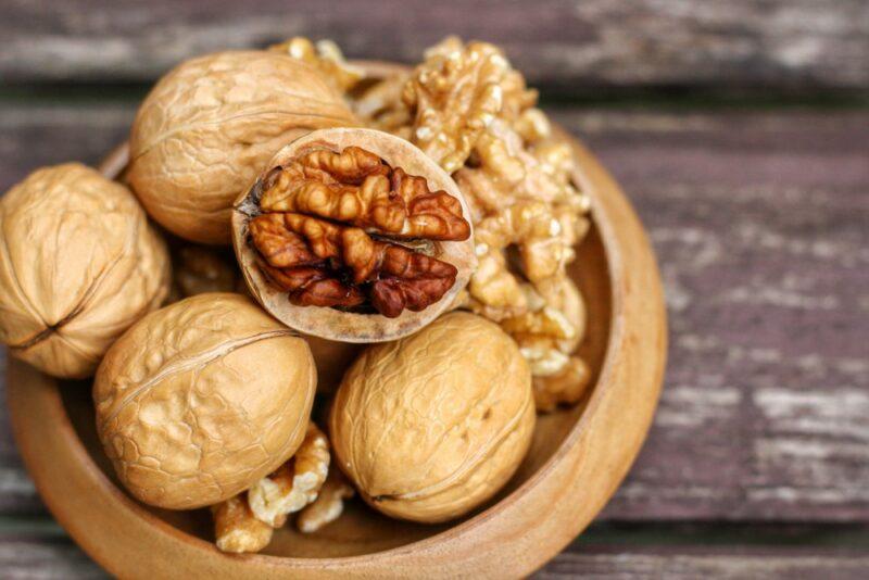 A brown wooden bowl with walnuts, one of which has been opened, on a wooden table