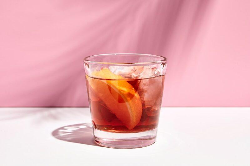 A white table containing a small little Venice cocktail against a pink background