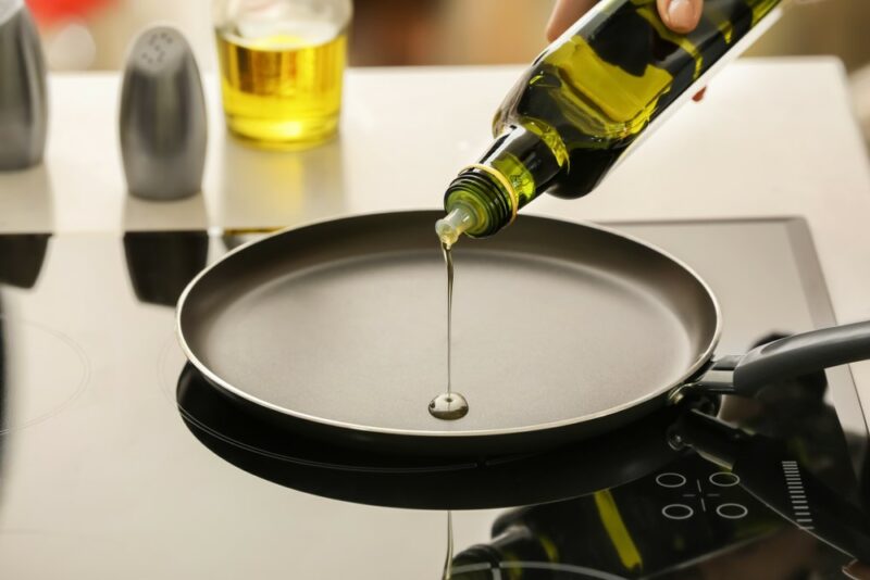 A black fry pan that someone is pouring a little olive oil into