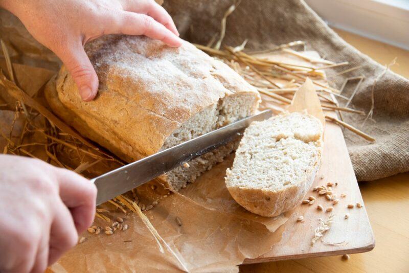 Someone with a loaf of sourdough that they're cutting