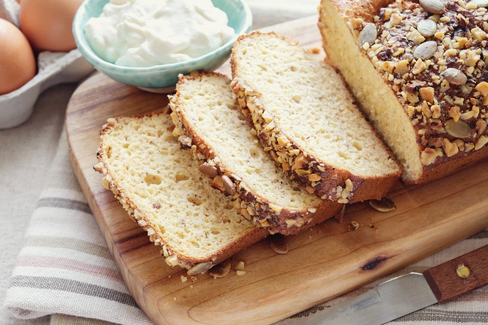 A wooden board with a loaf of keto bread next to eggs and sour cream