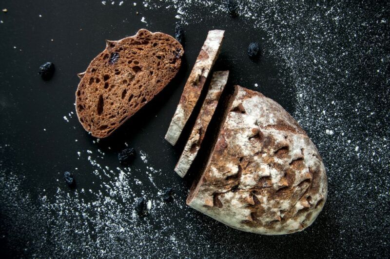 A black table with a loaf of rye bread covered in flour. Some of the loaf has been sliced