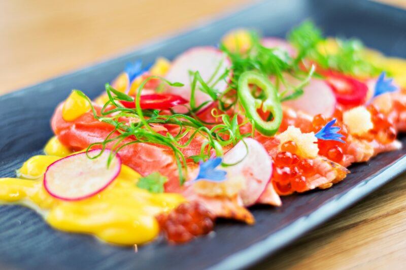 A blue dish with a meal called tiradito, which includes radishes and raw fish