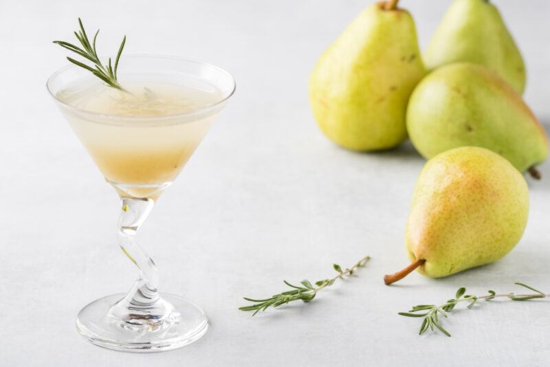 A lotus blossom martini garnished with rosemary, next to four pears