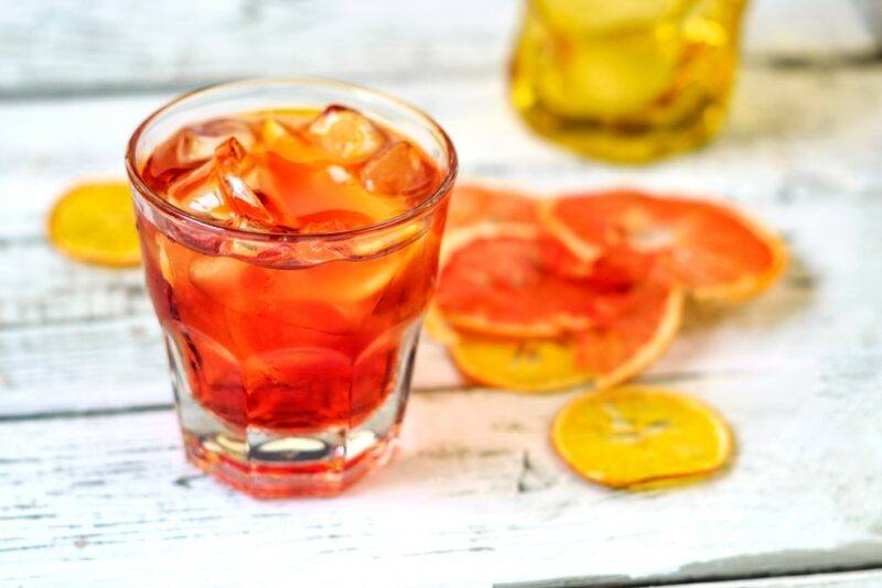 A glass containing a make it count cocktail on a white table that's been scattered with thin slices of orange and lemon