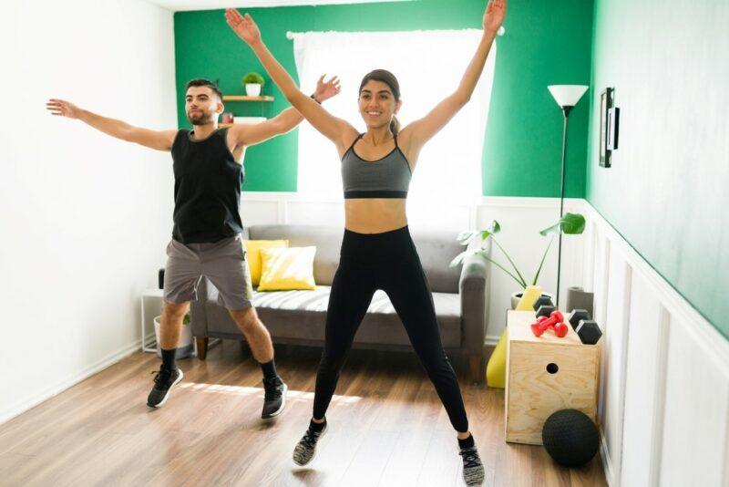 Two people exercising at home by doing jumping jacks